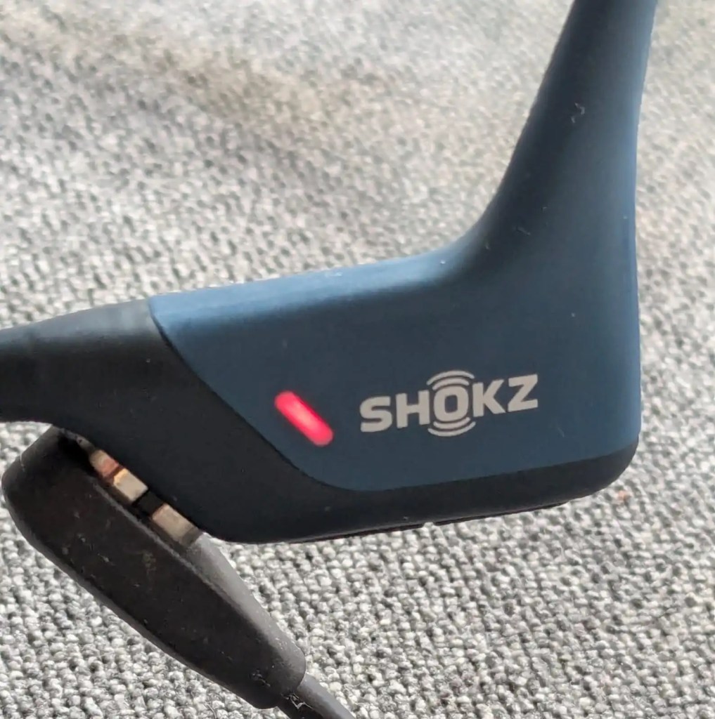 Close up of the magnetic Shokz OpenRun Pro charger charging the blue Shokz OpenRun Pro.